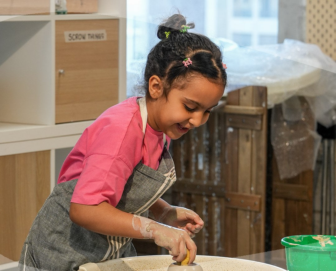 A young girl shaping a pot on the potter's wheel at a Ceramic Cube kids pottery workshop, Doha
